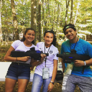 Three teenagers posing for a smile while playing laser tag in the woods.